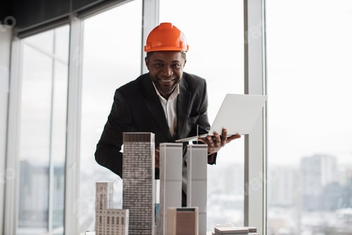 Preview: Focused african inspector using laptop inspecting skyscraper model in architectural modern office