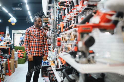 Preview: African american man holding and choosing electric screwdriver, standing in construction store