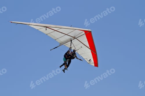 Preview: Amazing shot of human flying on a hang glider isolated on a blue sky background
