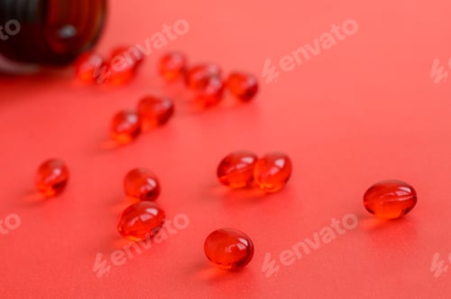 Preview: A lot of transparent red tablets were scattered from a small glass brown jar on a red surface