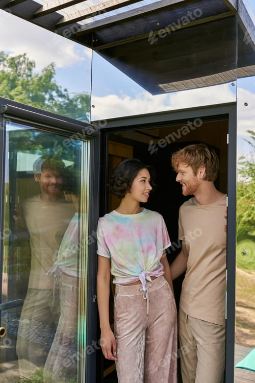 Preview: happy asian woman looking at redhead boyfriend while leaving home, standing near entrance together