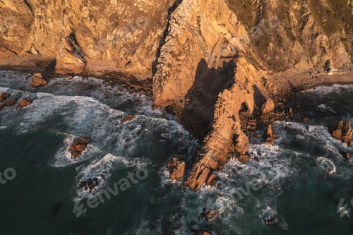 Preview: Foamy waves crashing on rocky cliffs at sunset