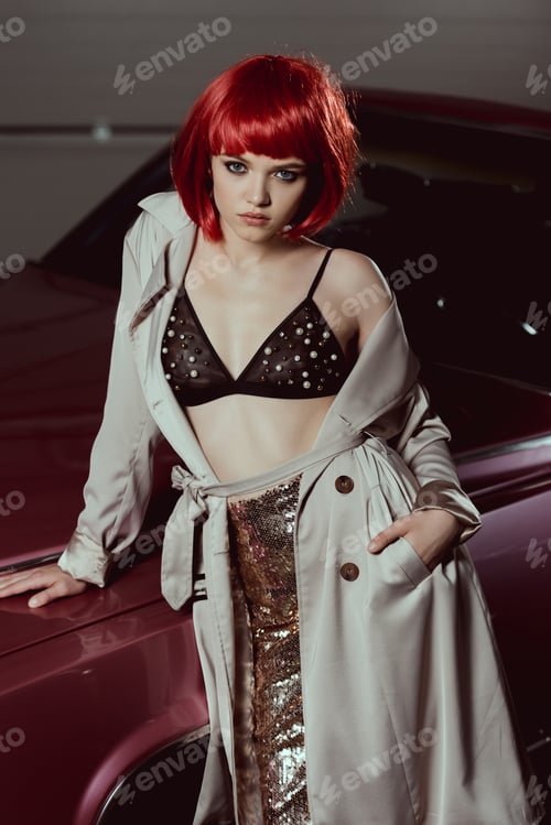 Preview: high angle view of stylish girl in trench coat and bra leaning at car and looking at camera