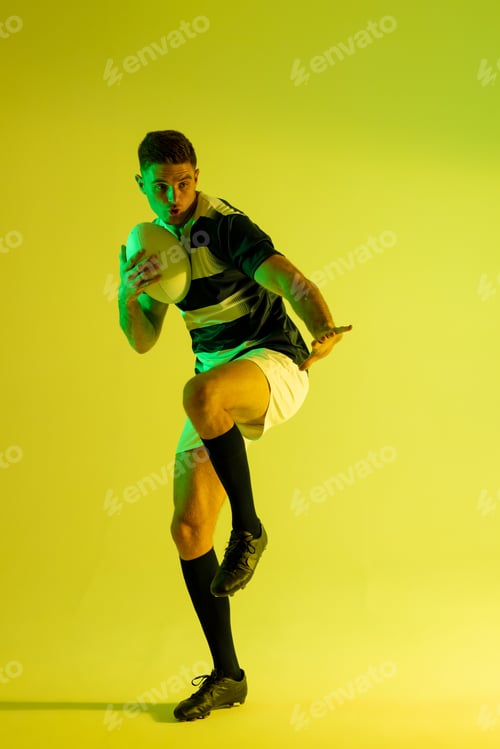 Preview: Caucasian male rugby player with rugby ball over yellow lighting