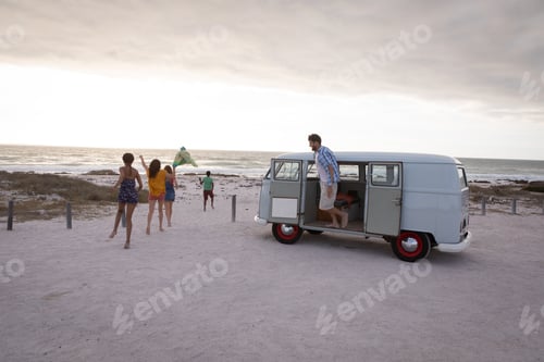 Preview: Side view of a Caucasian man getting down of a camper van against his friends walking towards beach