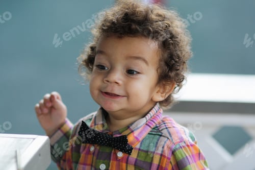 Preview: A cute little boy with dark curly hair stands on the street, looks into the distance, front view.