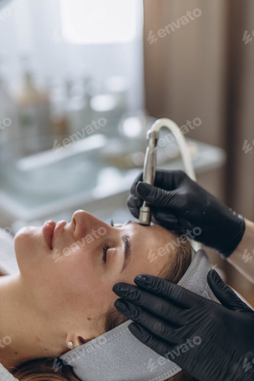 Preview: Professional dermatologist in medical gloves performs microdermabrasion on woman in a beauty salon