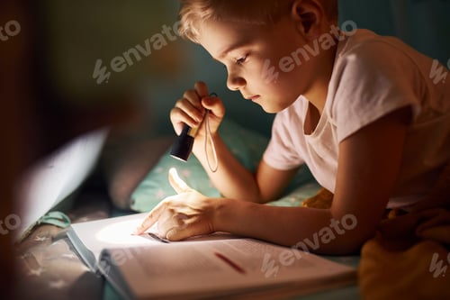 Preview: Reading book and using flashlight. Young boy in casual clothes lying down near tent at evening time