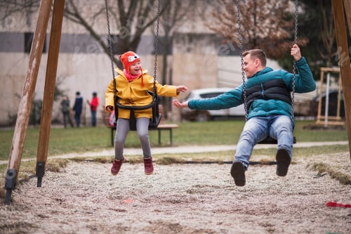 Preview: Father with his little daughter with Down syndrome on swings outdoors in playgraound.