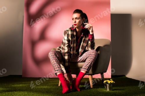 Preview: attractive elegant girl in checkered suit posing in armchair on pink background