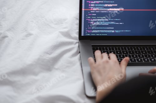 Preview: Young female programmer writes program code on a computer laptop in the bed at home. remote work