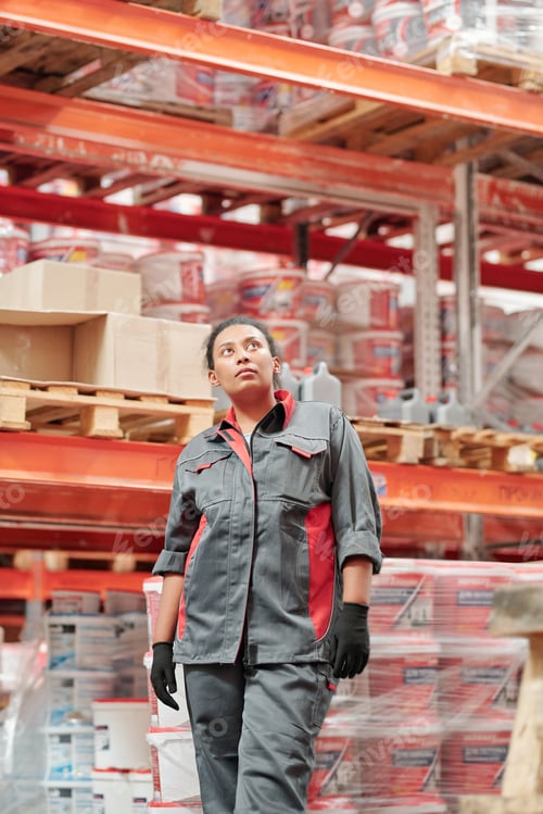 Preview: Young female worker of contemporary warehouse in uniform and gloves