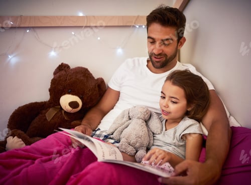 Preview: Cropped shot of a father reading a book with his little daughter in bed at home