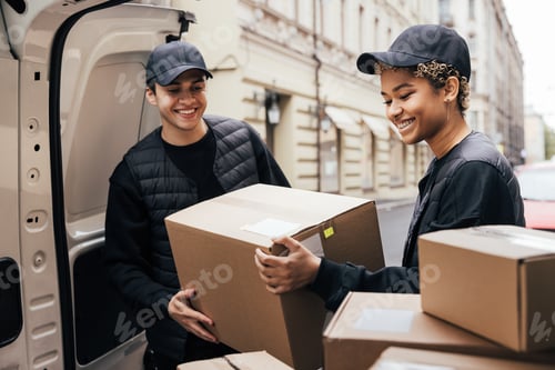 Preview: Two smiling couriers unloading cardboard boxes from van in the city