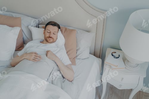 Preview: Handsome young bearded man sleeping in spacious comfortable bed