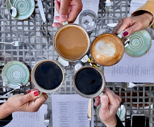 Preview: Four friends at breakfast with their coffee & latte at the table at a restaurant celebrating the day