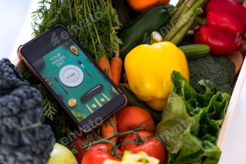 Preview: Top view wooden box with fresh vegetables and phone with Vegan diet mobile app