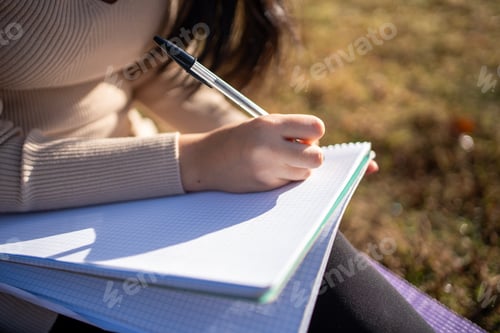 Preview: Student writing notes outdoors in sunlight with pen and notebook