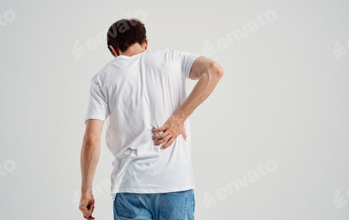 Preview: a man in a white t-shirt touches his back with his hand spine pain