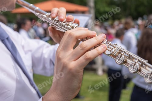 Preview: close-up view of a musician's hands playing a flute at an outdoor concert