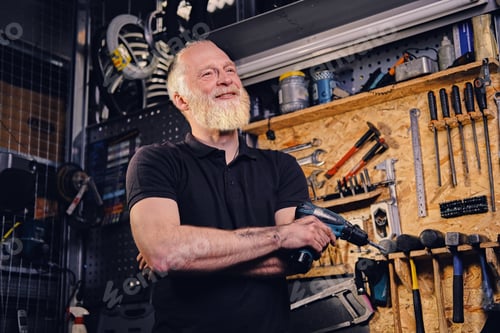 Preview: Joyful elderly man craftsperson with drill around bench