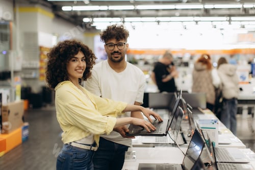 Preview: Smiling Couple Exploring Laptops Together in a Modern Electronics Store