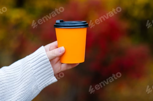 Preview: Female hand in white knitted sweater holding orange paper cup