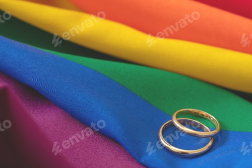 Preview: LGBT Gay marriage. Pair of golden rings on rainbow color textile, close up view. Copy space