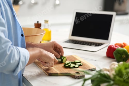 Preview: Man making dinner while watching online cooking course via laptop in kitchen, closeup