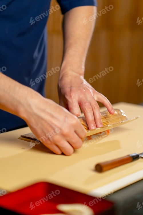 Preview: close-up in a Japanese restaurant a chef in a blue uniform on a yellow board spins a fish roll