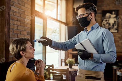 Preview: Waiter measuring guest's temperature with infrared thermometer in a cafe.