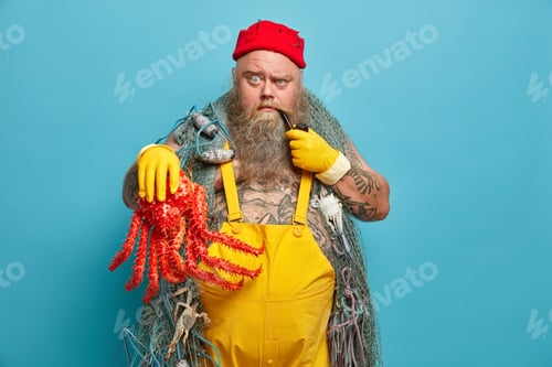 Preview: Indoor shot of serious bearded sailor raises eyebrows and looks strict at camera has tattooed body d