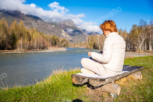 Preview: Woman playing a Tibetan singing bowl near mountain river