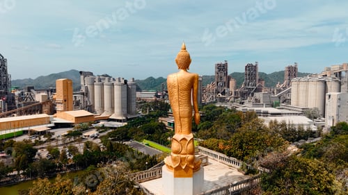 Preview: Golden buddha statue overlooking industrial cement factory development in thailand