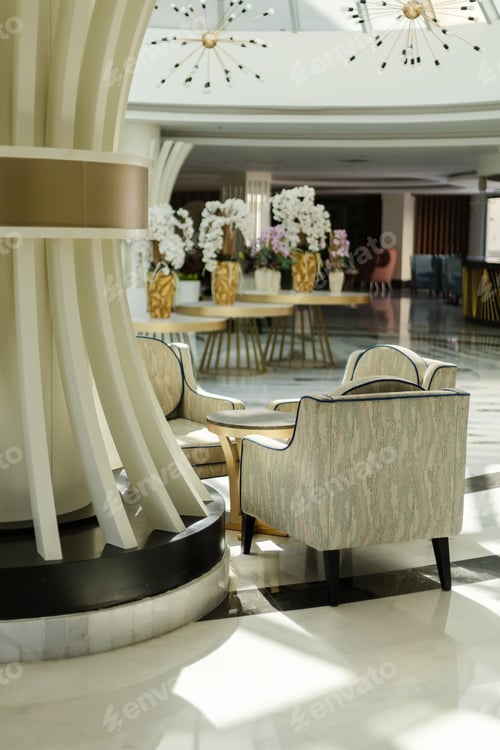 Preview: Chairs sit near a column in a hotel lobby, with decorative plants in the background.