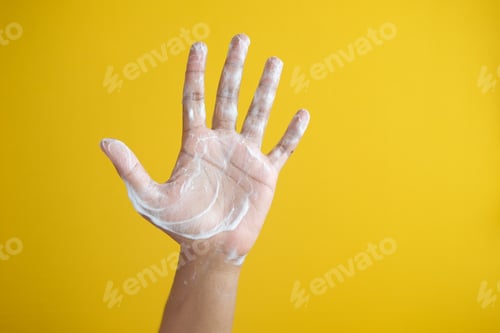 Preview: young man washing hands with soap against yellow background