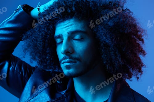 Preview: Portrait of fashion man with curly hair on blue background multinational, colored light, black