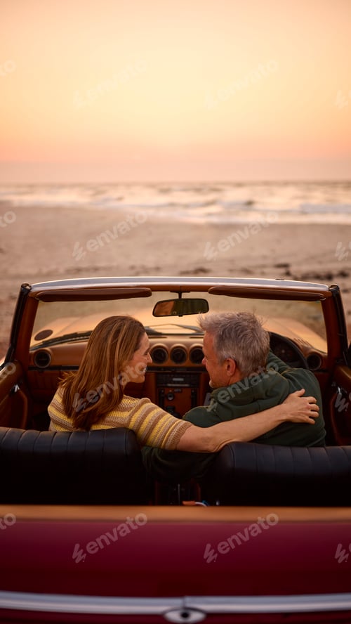 Preview: Rear View Of Retired Senior Couple On Vacation In Classic Sports Car At Beach Watching Sunrise