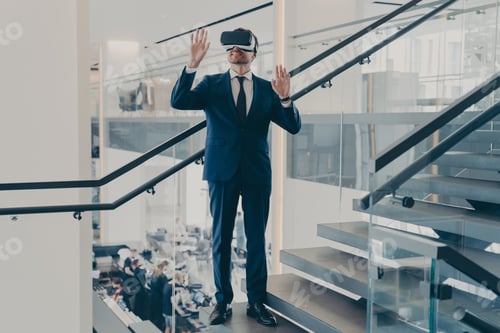 Preview: Businessman in VR headset stands on staircase in office lobby with hands up in air