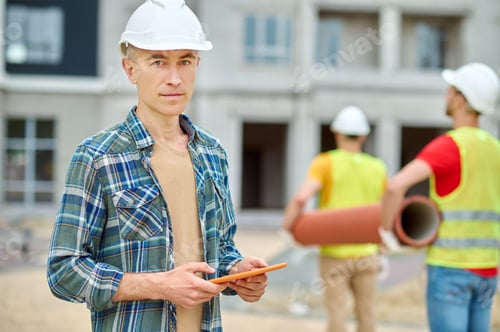 Preview: Man with tablet and workers carrying construction material
