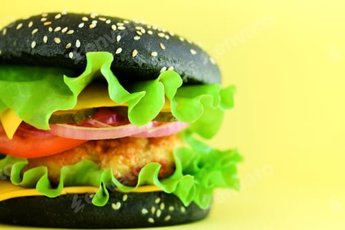Preview: Macro view of tasty black burger with beef, cheese, lettuce, onion, tomatoes on yellow background