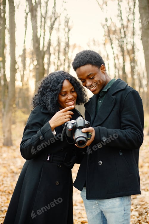 Preview: Black couple walking in park and looking in camera in their hands