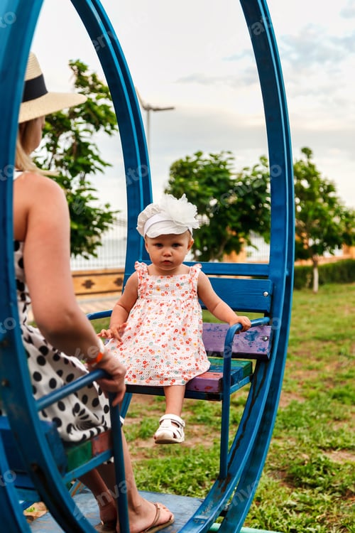 Preview: A little girl rides on a swing in the park with her mom