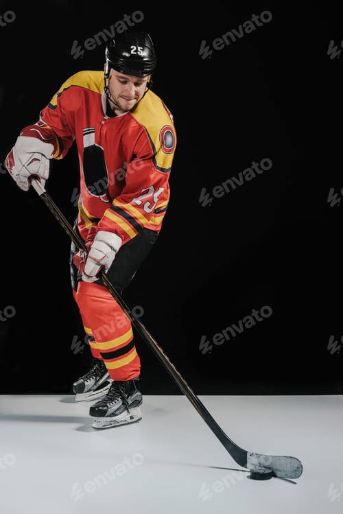 Preview: full length view of professional sportsman in skates playing hockey on black
