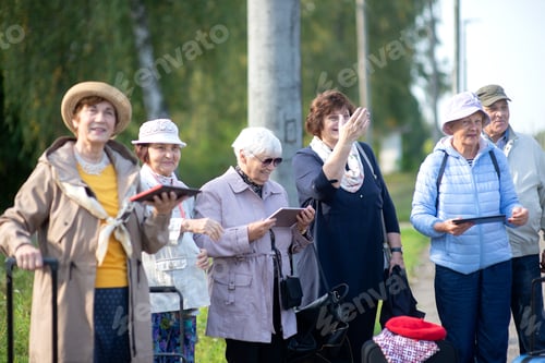 Preview: A group of happy senior friends with suitcases using tablet and waiting for a train on the platform