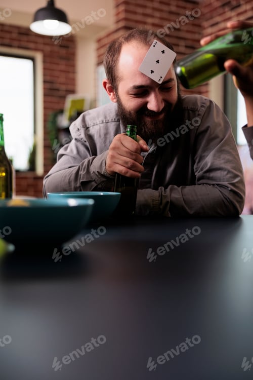 Preview: Cheerful man with plastic card on forehead laughing with friends while hanging out together.