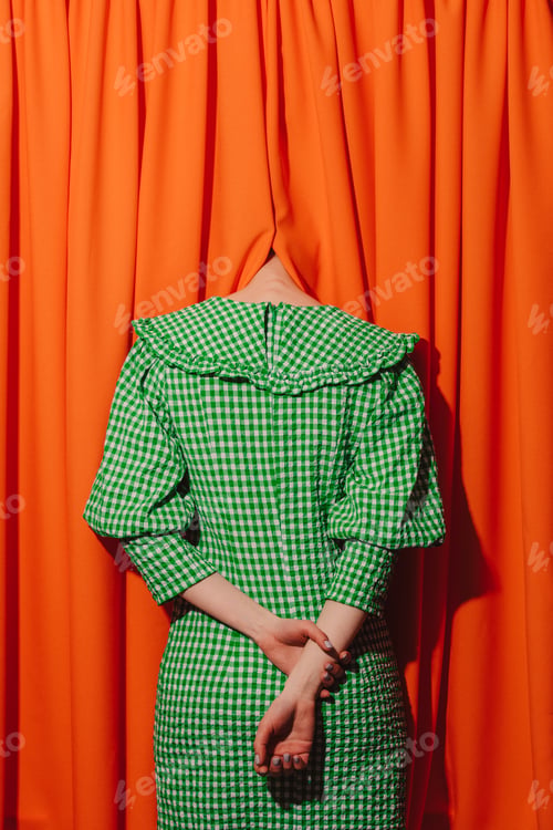 Preview: girl in a green dress hides her head in orange curtains