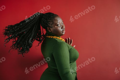 Preview: Beautiful plus size African woman with braided hair looking at camera on red background