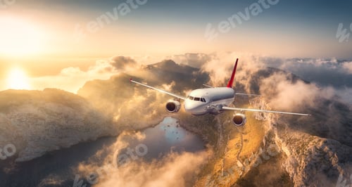 Preview: Airplane flying above mountains and low clouds at sunset