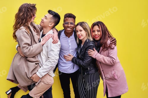 Preview: Multiracial young people having fun on yellow background. Group of friends of various ethnicities.